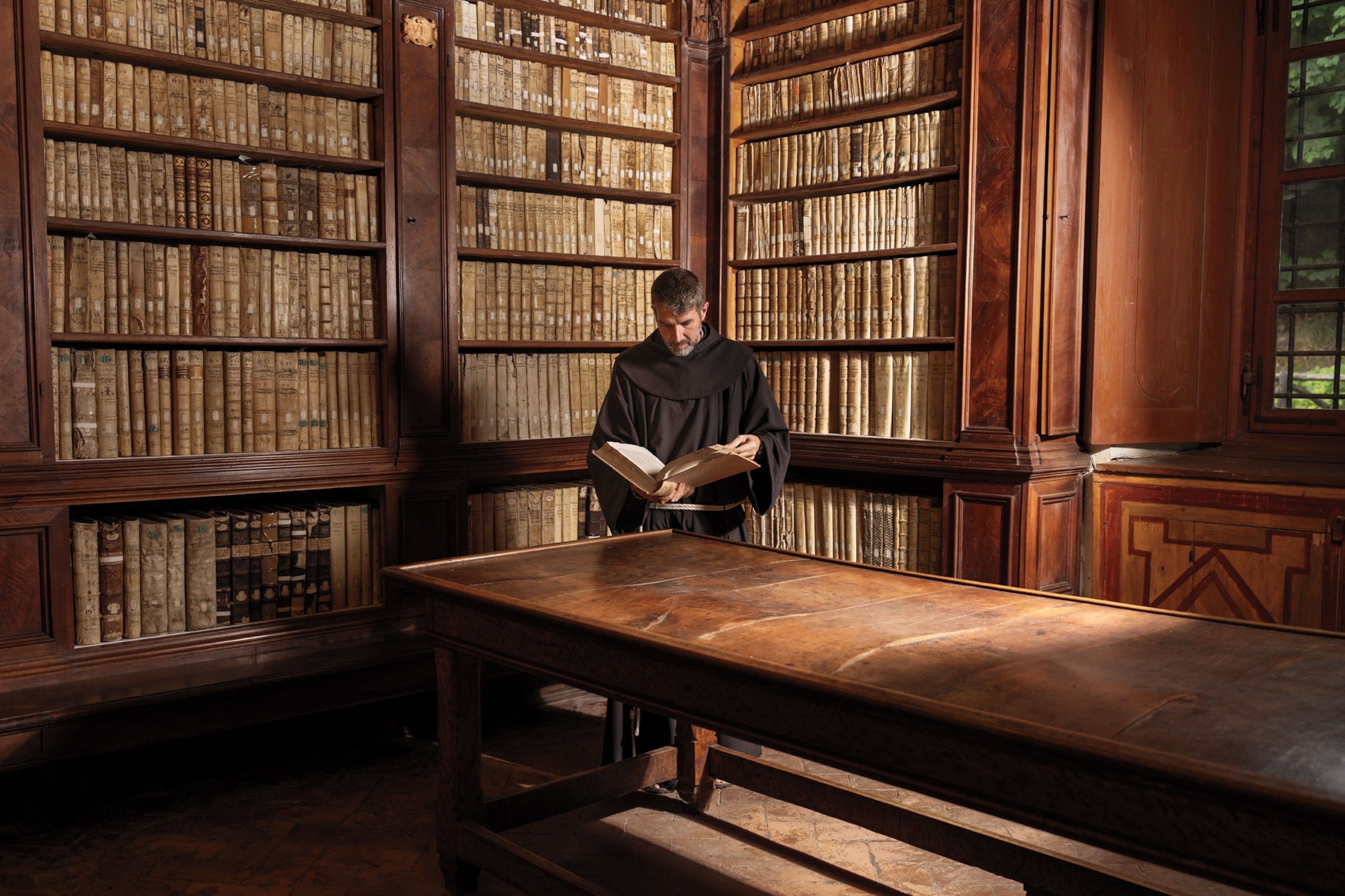 A monk reads a book inside a library.