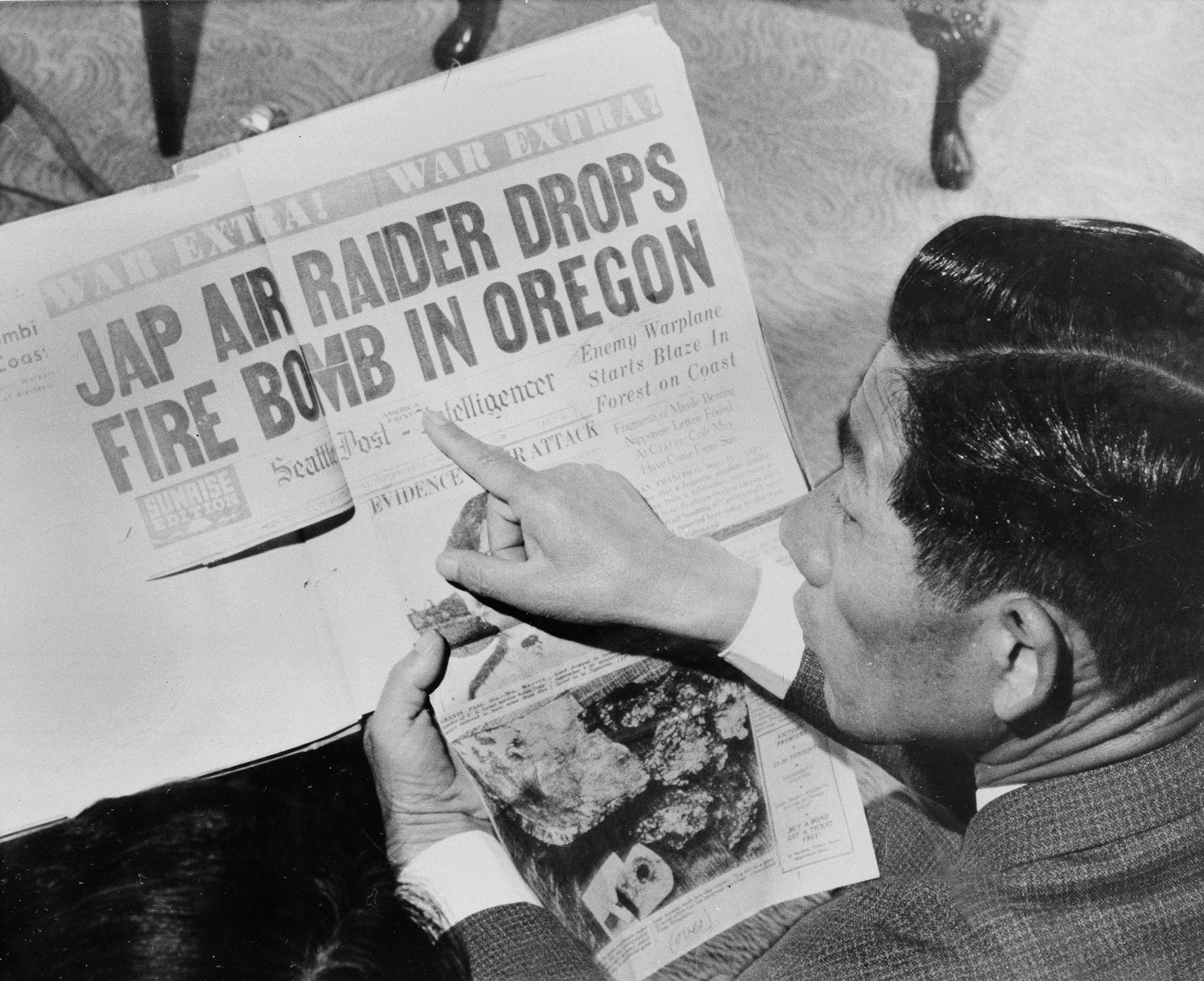 A man with slicked hair and looks at news paper.