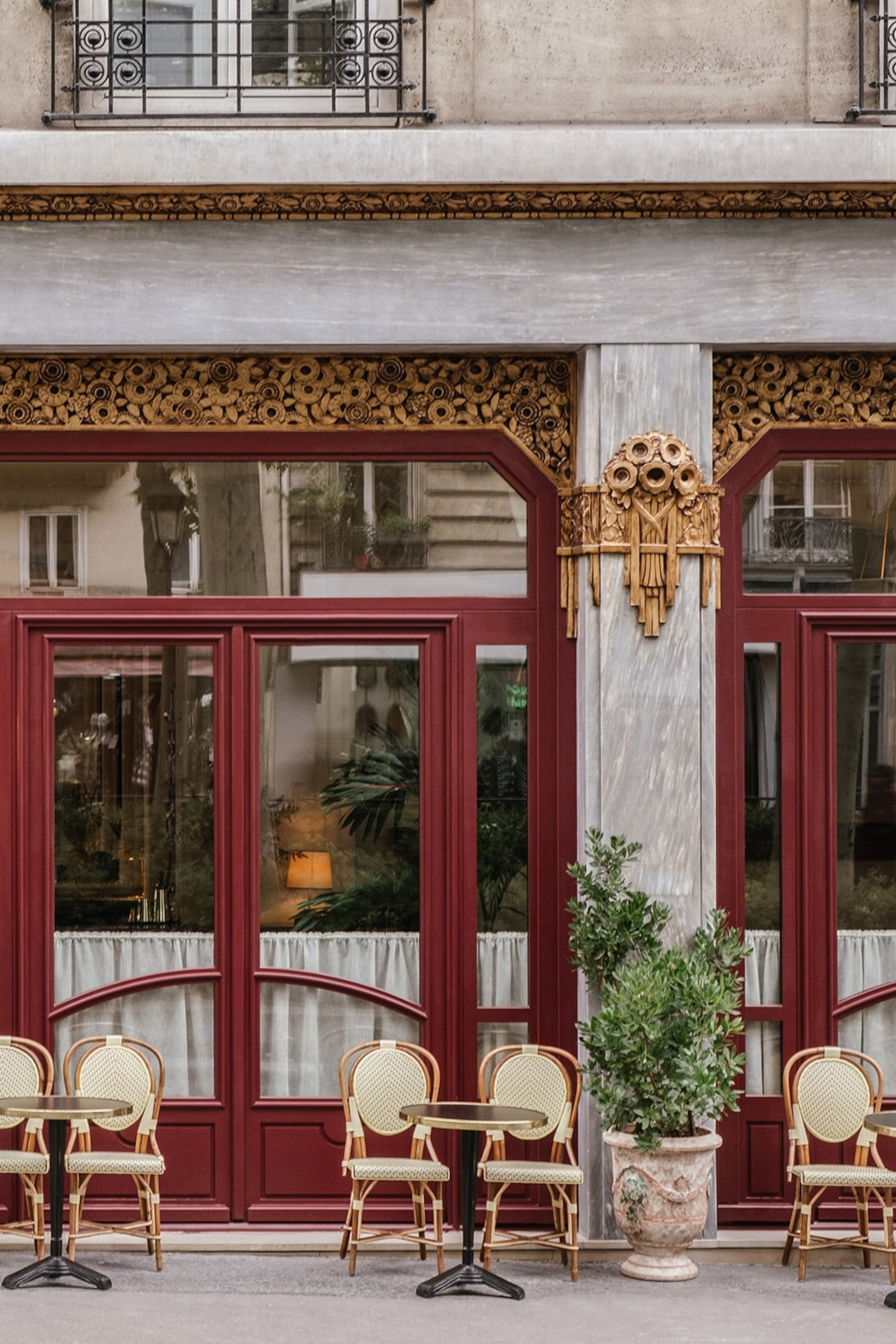 A traditional hotel-front in Paris. The window and door frames are painted a dark red, and wooden and cream chairs line the front.