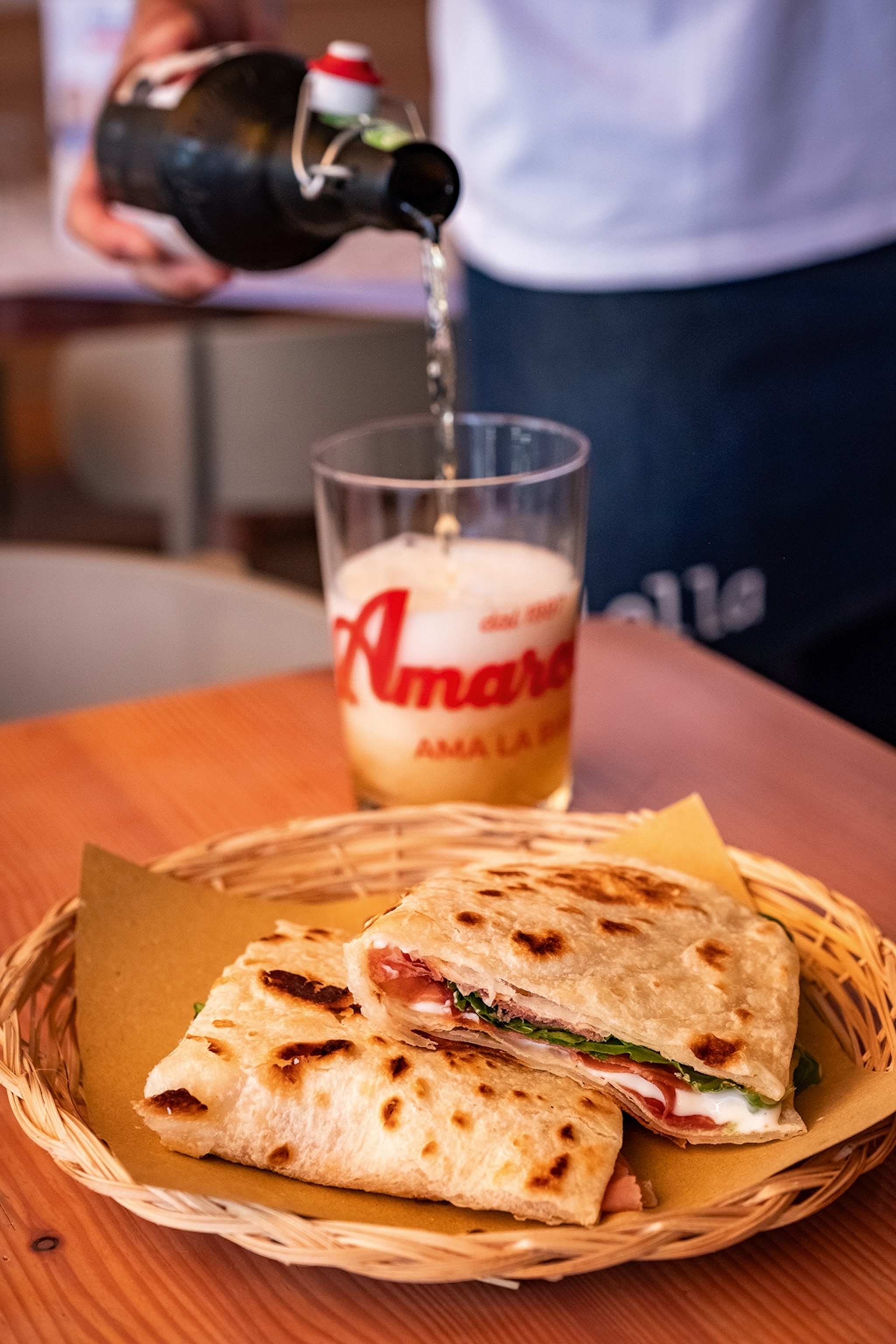 Flatbread filled with meat cheese and lettuce served in a shallow basket next to a glass of beer