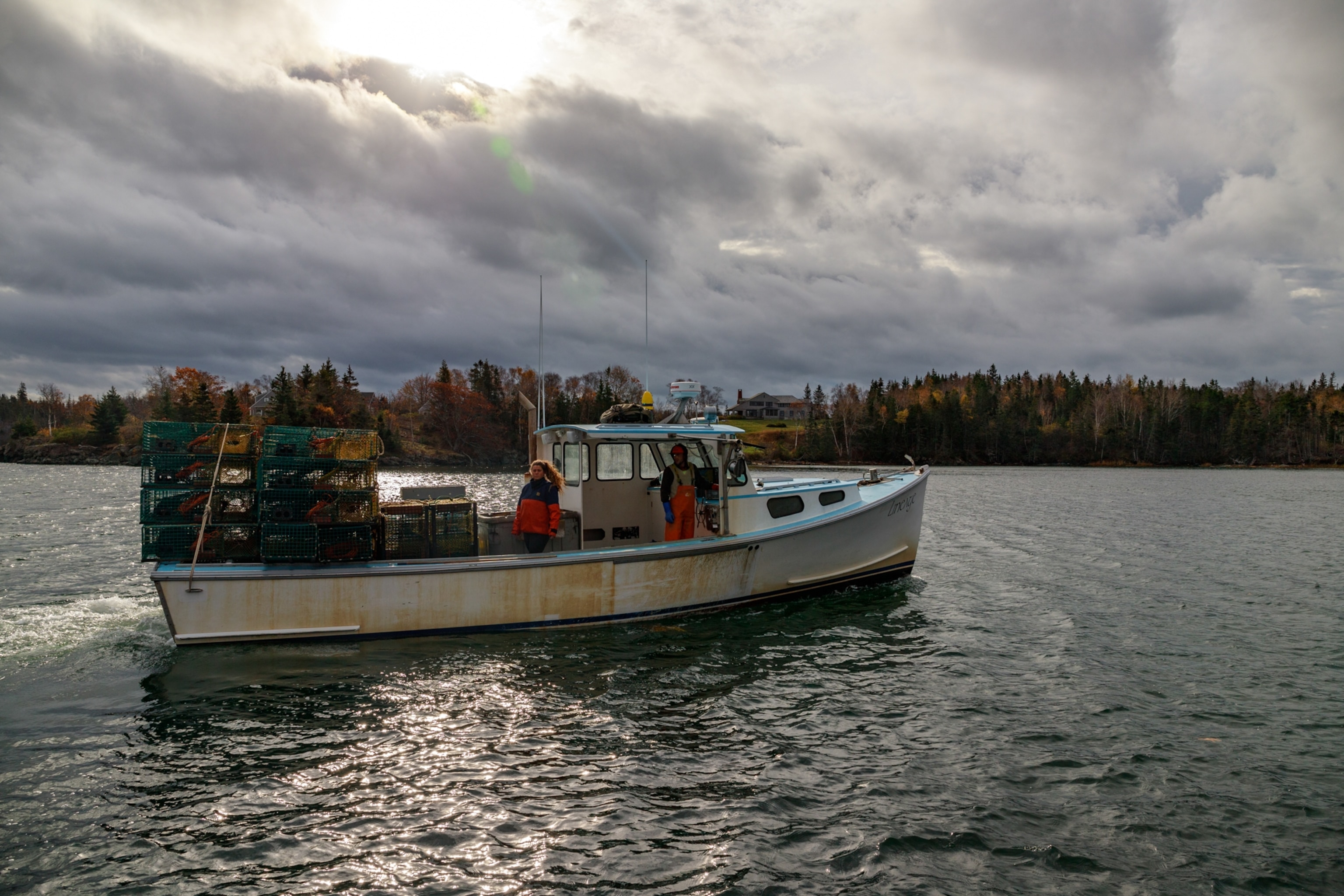 A fishing boat glides across the bay with lobster traps stacked on stern. North Haven Island, Maine, United States of America. 