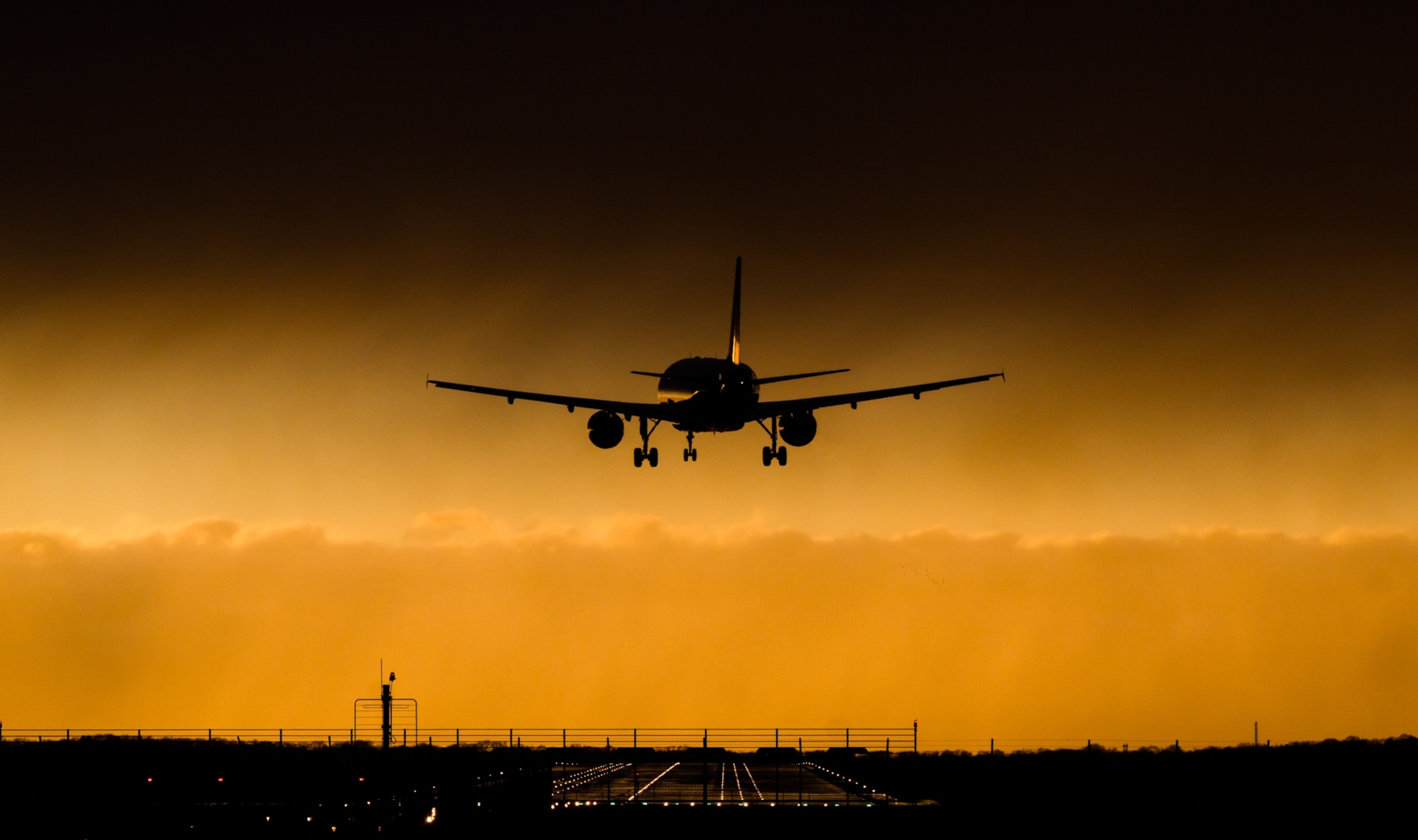 an airplane landing beneath a curtain of dark clouds; the plane is crooked in its approach due to the high winds