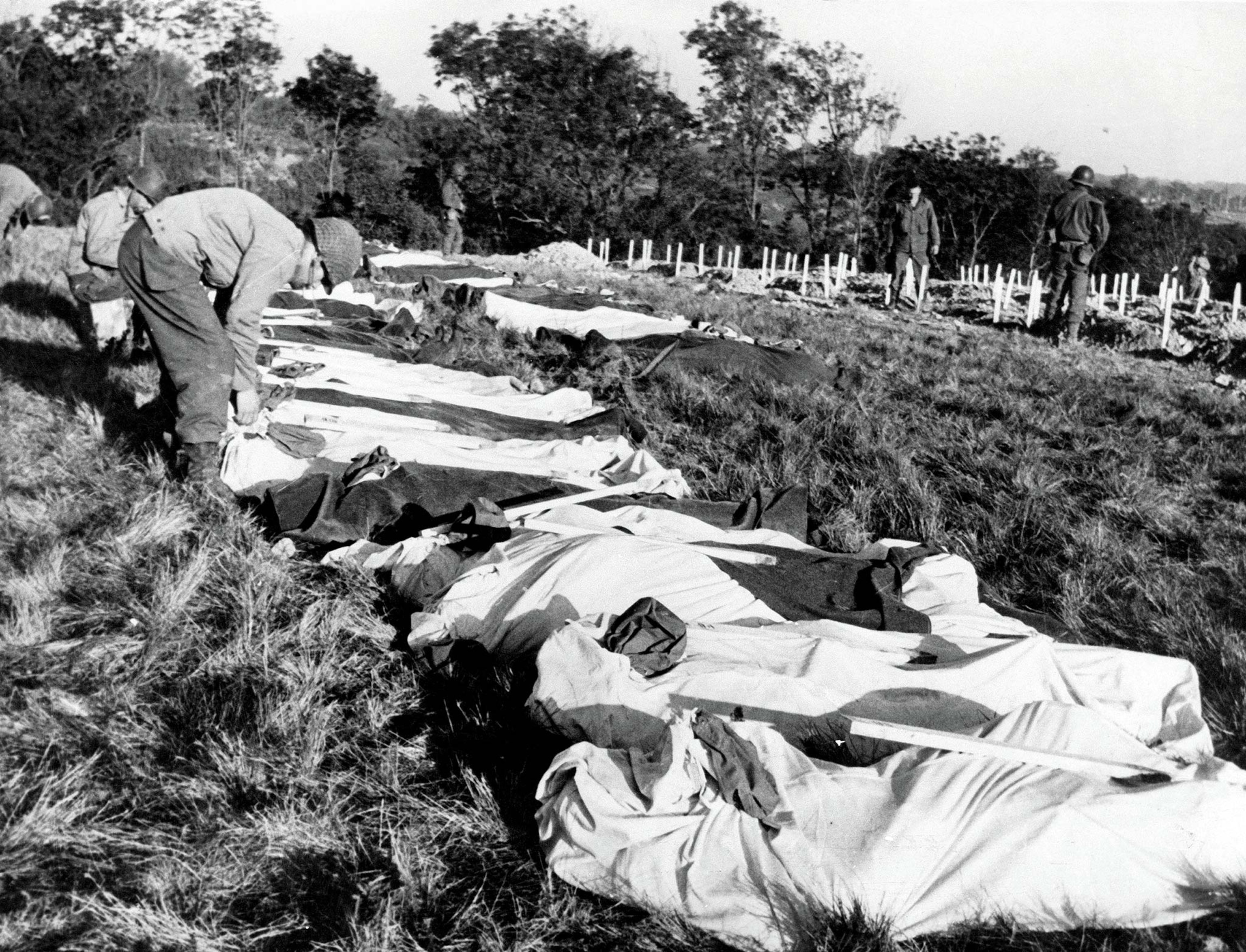 Soldiers' bodies are covered in fabrics in a makeshift graveyard