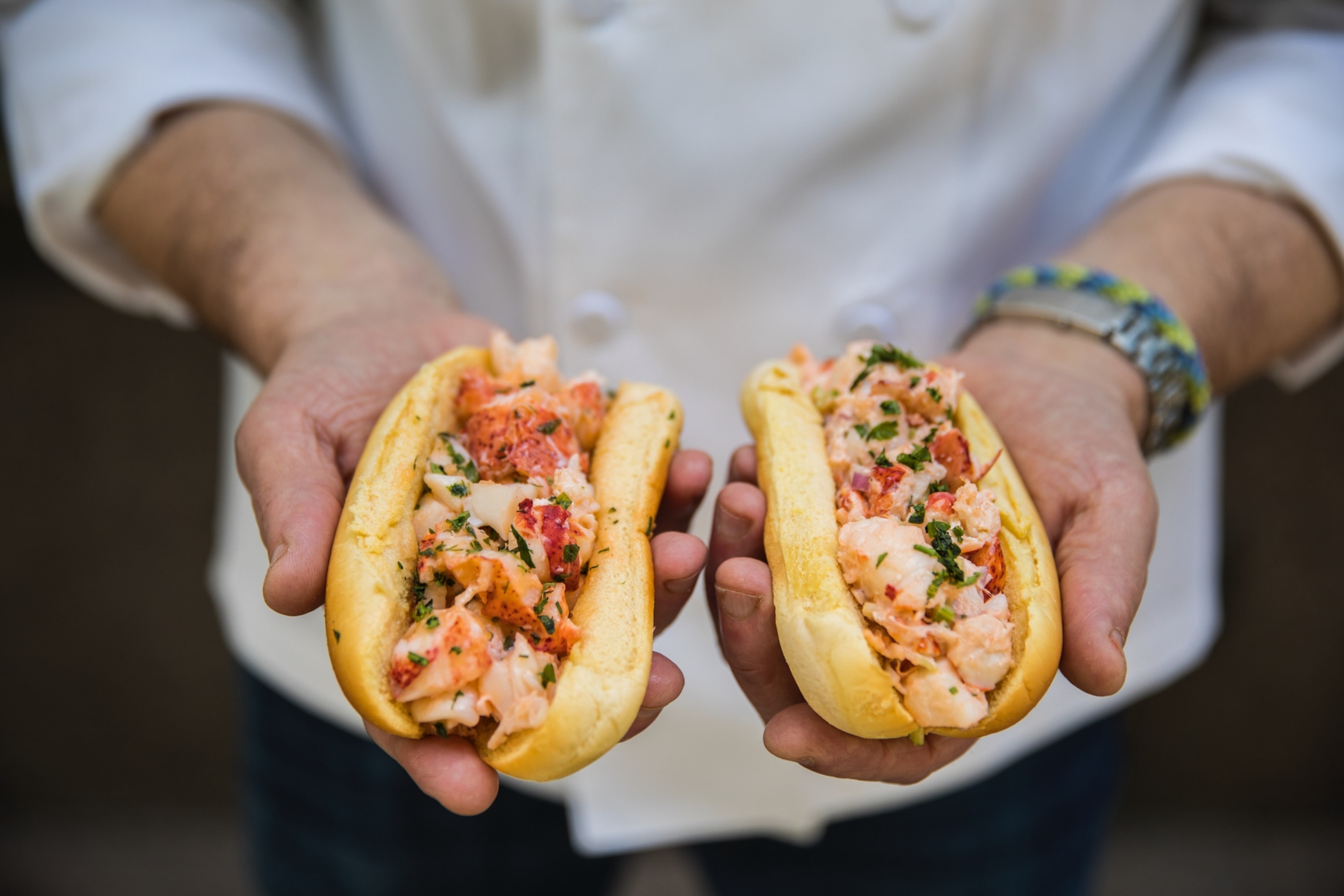 A man holds two lobster rolls in his hands.