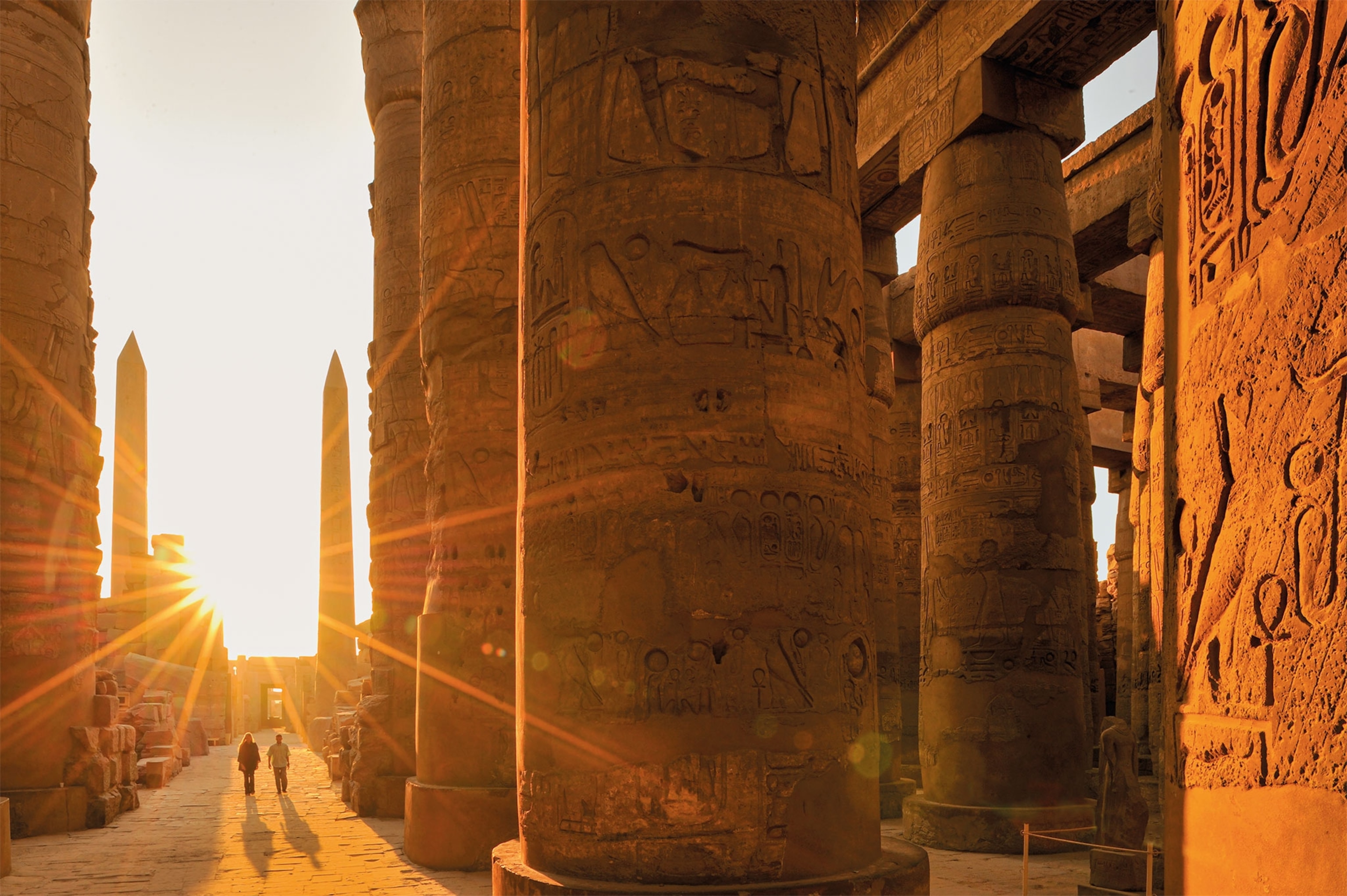 Two of three obelisks at the Temple of Amun at Karnak Temple Complex tower behind the Great Hypostyle Hall, with the sun shining in between