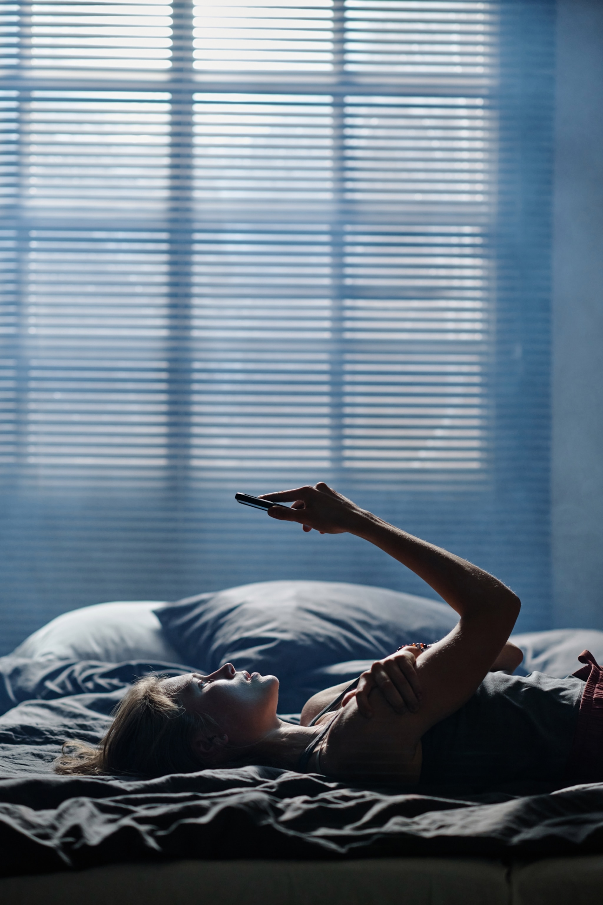 A young woman lying in bed with a serious expression while looking up at her phone