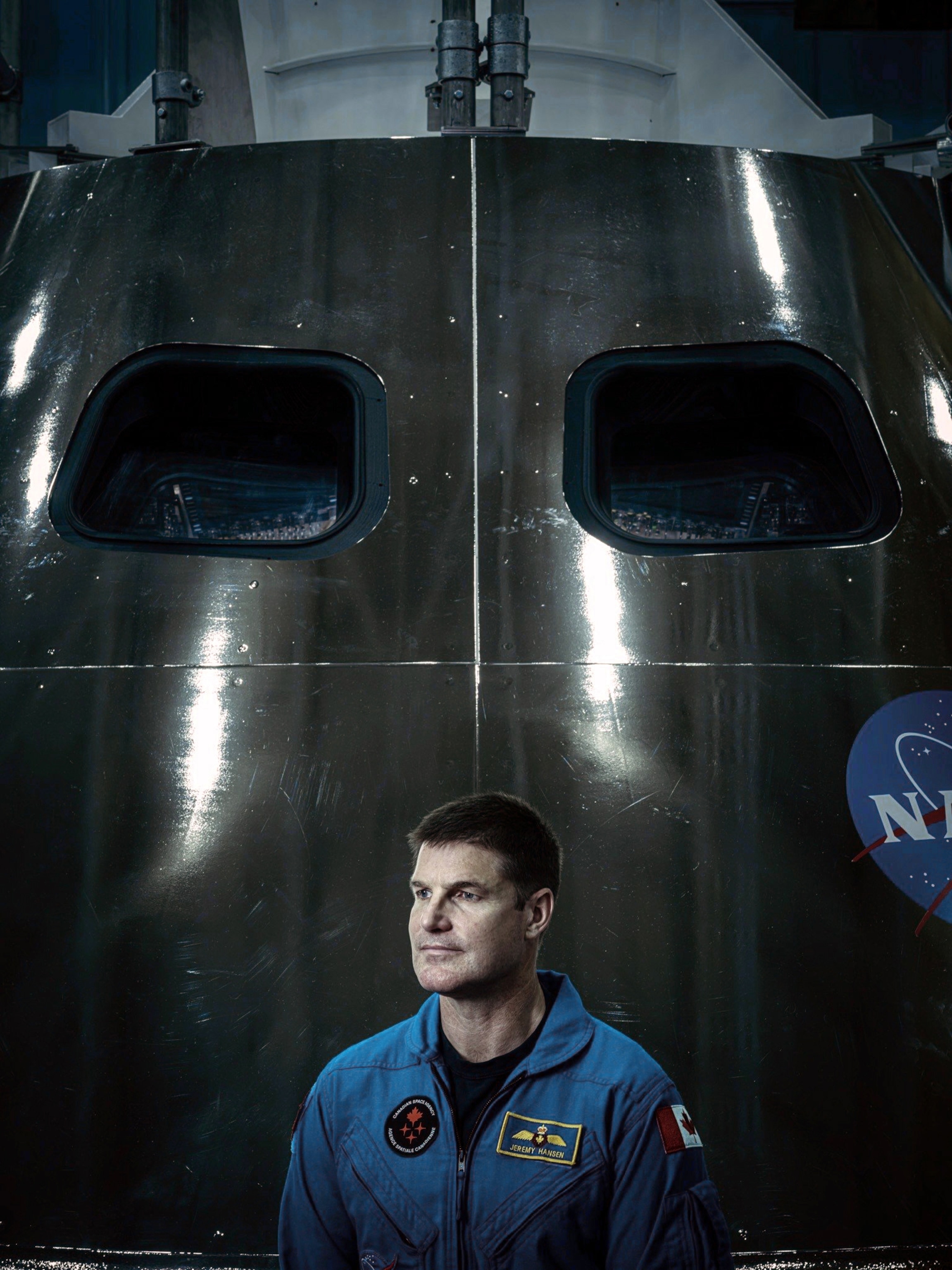 Portrait of a man in blue flight suit on the background of spaceship cockpit with two round windows.