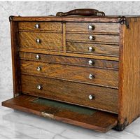 Antique Quartersawn Oak Machinist Chest Tool Box, c. Early 20th Century      - Pairs Nicely with Many Traditional & Eclectic Interior Styles     - Crafted of Solid Oak with an Attractive Quartersawn Grain Throughout     - Raised Panel Drop Down (and Store Away) Front     - Misc Sized Storage Drawers with Nickel Pulls     - Original Aged Leather Top Handle     - Exposed Joinery Corners with Decorative Ormolu Mounts     - Unsigned or Marked