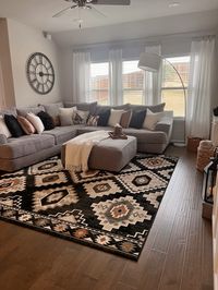 Grey couch, western rug, black clock, brown leather pillows.