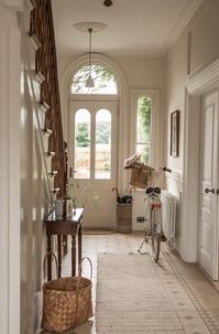 A modern take on Victorian decor. Cozy entrance with white bicycle. Beige walls, window with a view, rustic decor, and a calm, inviting mood.  In this article we will share how to transform your living space into a modern Victorian masterpiece and make it a true reflection of your personality. Cottagecore Image by Nicola Houthwaite