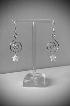 a pair of silver earrings sitting on top of a glass display stand in front of a white wall