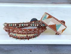 This sparkly, loom woven bracelet features an earthy neutral brown, tan, turquoise, and silver color palette. The pattern and loom work is all original and hand crafted by me. It can be customized to your favorite colors, simply send me a message at checkout with your color preferences.  The bracelet is approximately 1 inch wide and 6.5 inches long. The leather wrap can include extra clasp lengths allowing this bracelet to be one size fits most. If you have any questions or if you would prefer another color combination please feel free to ask. The bracelet is created by hand using high quality Japanese Delica seed beads and genuine leather cording. The clasp is a silver plated pewter button. *Each item is carefully hand crafted. Because of our passion and desire to create the best possible Handmade Earthy Friendship Bracelets, Brown Beaded Southwestern Jewelry, Earthy Brown Beaded Bracelets With Round Beads, Southwestern Brown Beaded Jewelry, Artisan Wrap Bracelet With Round Beads, Southwestern Style Brown Beaded Jewelry, Brown Beaded Friendship Bracelets As Gift, Beaded Brown Friendship Bracelets As Gift, Adjustable Brown Bohemian Beaded Bracelets