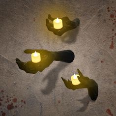 two hands holding lit candles on the ground