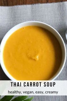 thai carrot soup in a white bowl on a table with spoons next to it