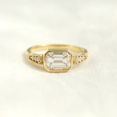 a yellow gold ring with an emerald stone and two diamonds on the band, sitting on a white surface