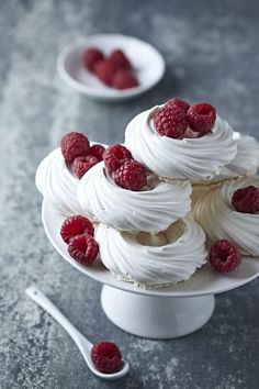 a cake with white frosting and raspberries on top sitting on a plate