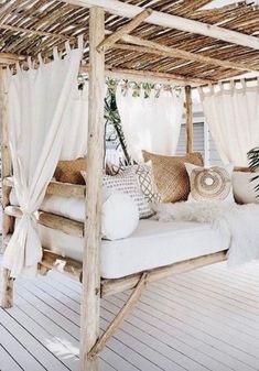 a canopy bed with white curtains and pillows on top of it in the middle of a porch