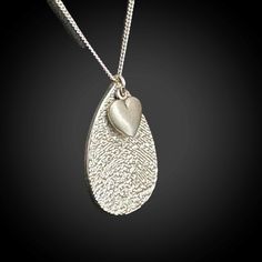 Our Fingerprint Jewelry is a personal and meaningful keepsake that will provide a constant reminder of your loved ones, whether they are with you in the present or present only in your memories. Simply provide us with the fingerprint and we will create a unique impression on a Sterling Silver Teardrop necklace, measuring approximately 7/8" in length. As an added touch, we also include a heart charm, measuring approximately 1/4". This necklace will be a cherished item for many years to come.   Our specialized process recreates your loved ones' fingerprints, providing a recessed texture that allows you to feel every intricate detail of the imprint.  OPTIONS:  ADD PERSONALIZED TEXT OR HANDWRITING ON REVERSE SIDE. Using our state-of-the-art infrared laser technology, we can expertly engrave th Teardrop Heart Charm Jewelry Gift, Sterling Silver Teardrop Jewelry With Heart Charm, Personalized Silver Teardrop Jewelry, Heart-shaped Engraved Jewelry For Remembrance, Gift Teardrop Necklace With Heart Charm, Teardrop Heart Charm Necklace For Gift, Teardrop Necklace With Heart Charm For Gift, Teardrop Engraved Jewelry Gift, Heart Charm Teardrop Necklace For Gift