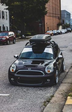 a small black car with luggage strapped to it's roof is parked on the street