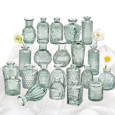 a collection of glass vases and jars on a white cloth with a flower in the middle