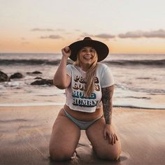 a woman sitting on the beach wearing a hat