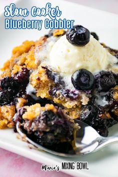 a white plate topped with blueberry cobbler next to a fork and ice cream