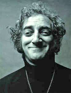 an old photo of a man with curly hair wearing a black shirt and smiling at the camera