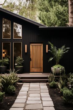 a black house with lots of windows and plants in the front yard, along with steps leading up to it