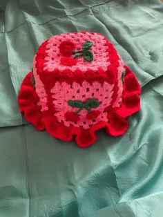 a crocheted red and pink bag sitting on top of a green sheet covered bed