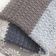 three crocheted blankets are stacked on top of each other, one is gray and the other is white