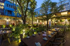 an outdoor dining area with tables and chairs, surrounded by greenery at night time