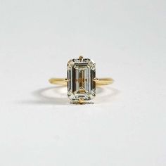 an emerald - cut diamond sits on top of a yellow gold band, with the center stone surrounded by smaller diamonds