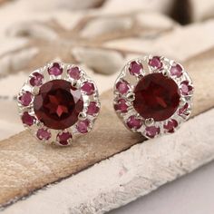 Harmonious pink and red gems come together on Bhavya Jain small but stunning stud earrings. The artisan crafts the earrings from rhodium-plated sterling silver, centering the pair with a single faceted garnet stone. A ring of deep pink rubies circle the garnet with sparkling beauty.