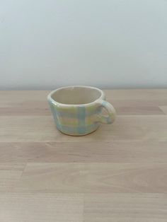 a small cup sitting on top of a wooden table next to a white wall and floor