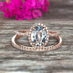 an oval shaped blue and white diamond ring on top of a wooden table with pink flowers in the background