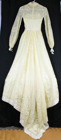 an old white dress is on display in front of a black backdrop and wooden floor