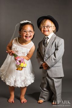 two young children dressed in suits and ties posing for a photo with their wedding bouquet