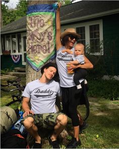 a man and woman holding up a baby next to a tree in front of a house