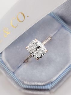 an engagement ring with a princess cut diamond in it's presentation box on display