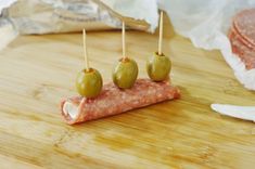 some green olives are sitting on top of a piece of meat with toothpicks sticking out of it