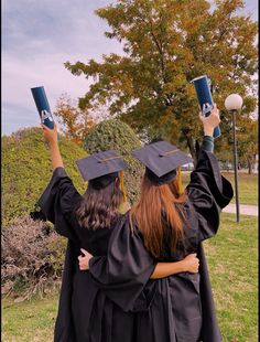 two women in graduation gowns holding up their hats