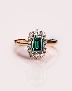 an emerald and diamond ring on a white surface