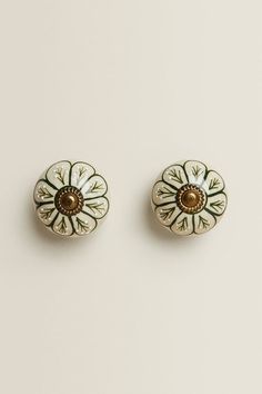 two white and gold flower shaped knobs on a white surface, one with a brown center