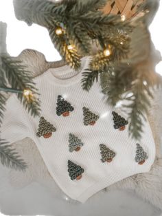 a teddy bear wearing a sweater with christmas trees on it next to a pine tree