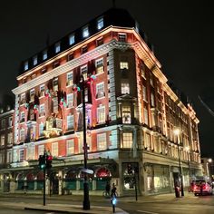 a large building lit up at night with christmas lights on it's windows and people crossing the street