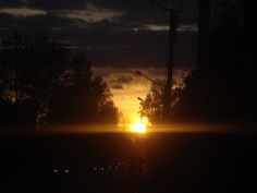 the sun is setting behind some trees in the dark sky with cars driving down the road