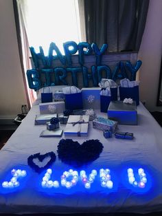 a birthday cake and presents on a bed with the words happy birthday lit up in blue