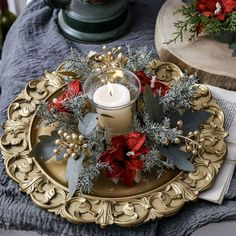 a candle is sitting on top of a gold plate with holly and poinsettis