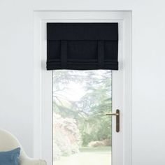 a white chair sitting in front of a window with black roman shades on the windowsill