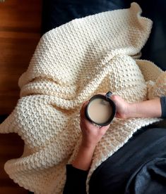 a person holding a cup of coffee under a blanket